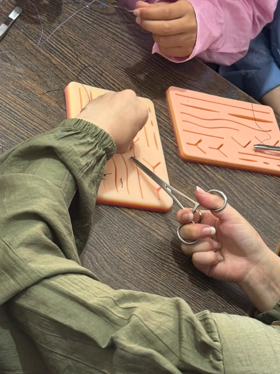 A student’s hand places a stitch on a practice pad