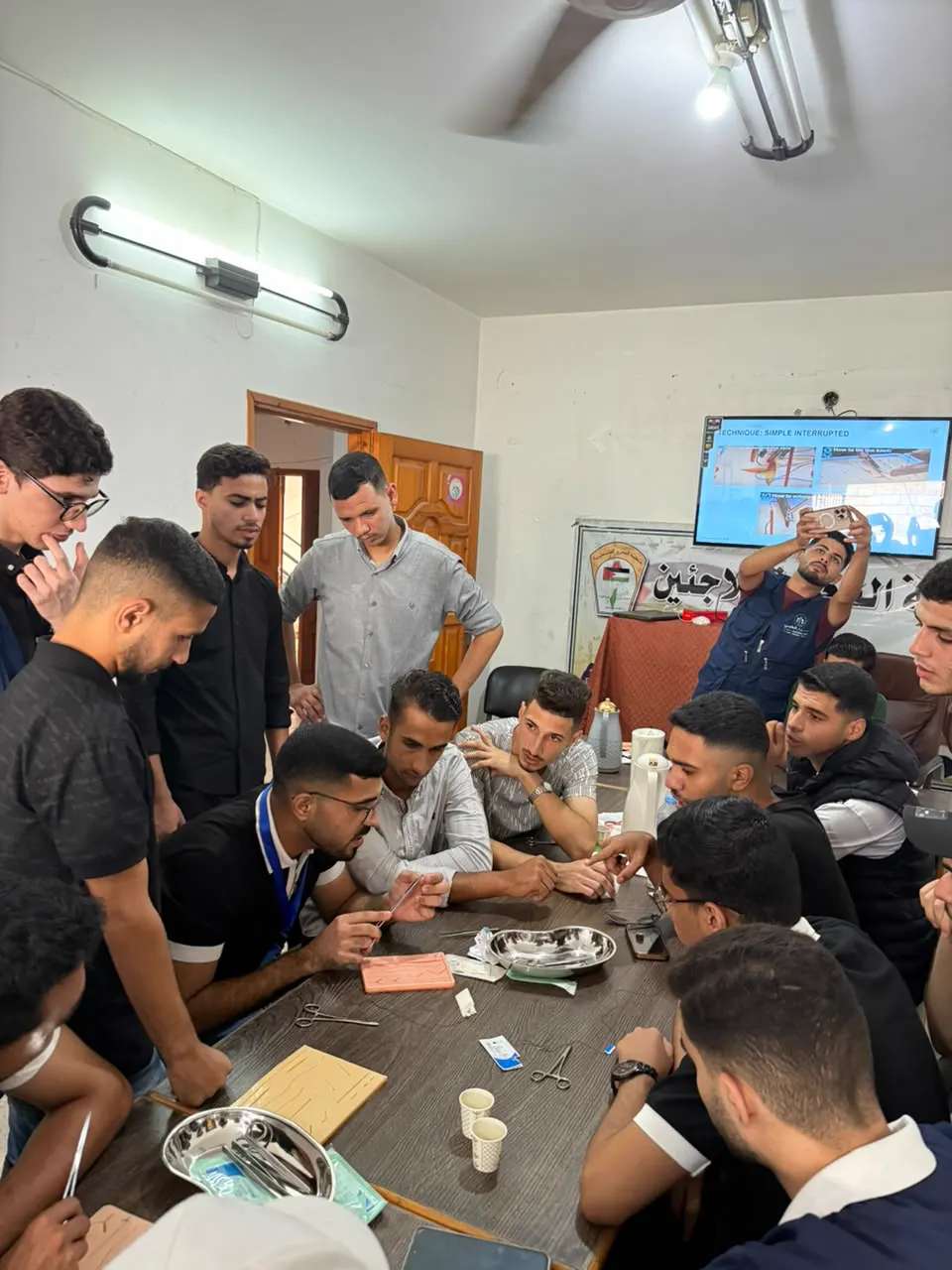 Students gathered around a table practising suturing while a trainer looks on