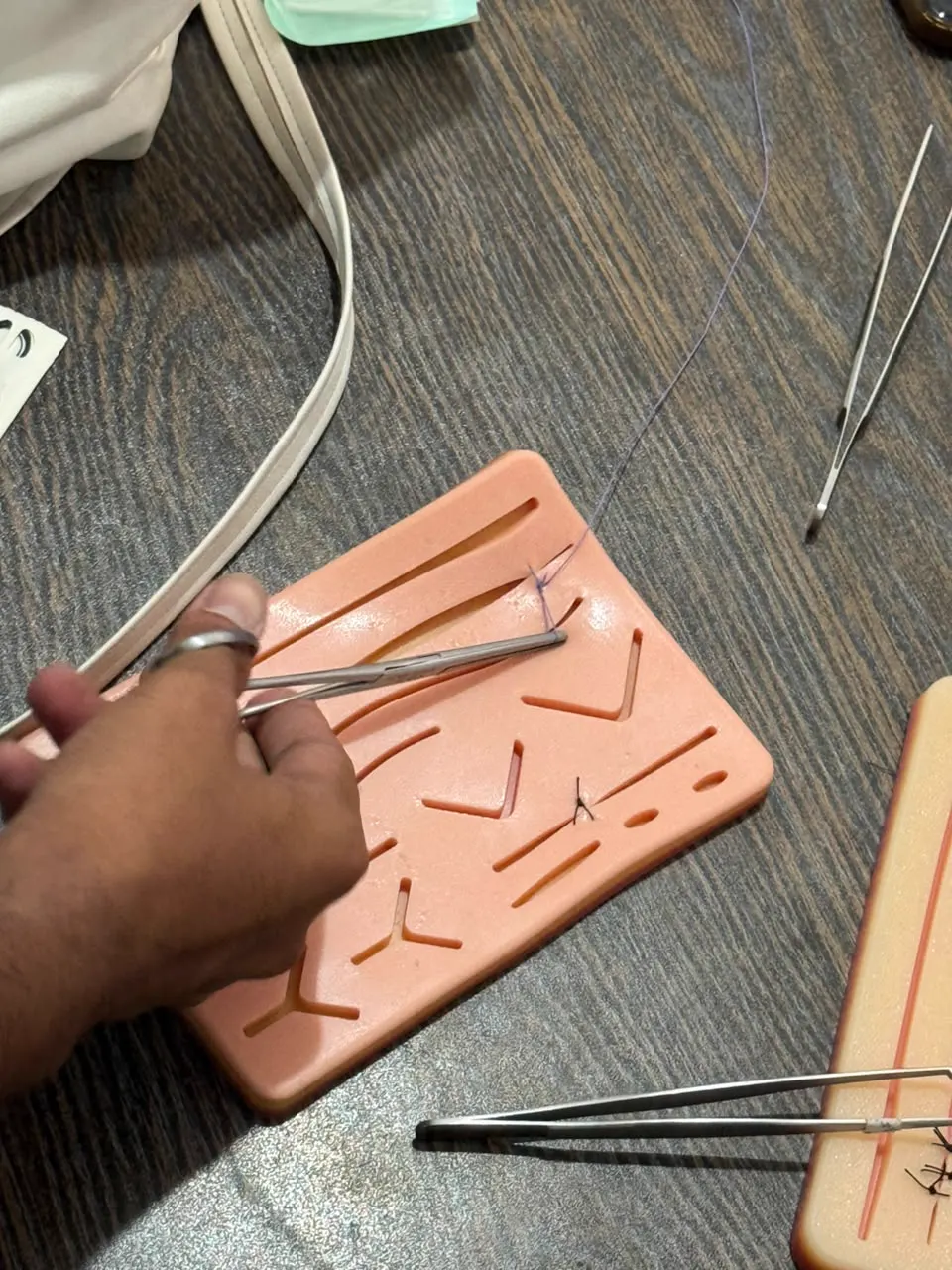 Hands suturing a practice pad with a needle holder and forceps