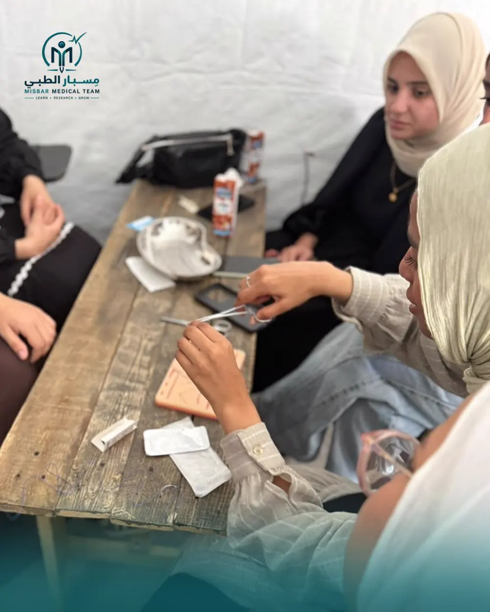 Students practising surgical suturing around a wooden table